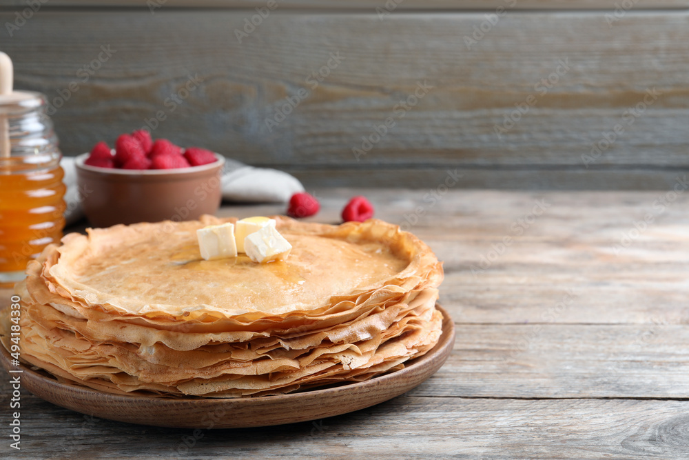 Stack of delicious crepes with melting butter on wooden table. Space for text