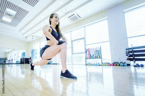 The girl is doing a warm-up in the gym. Fitness instructor with athletic body in sport club. Active lifestyle of a woman. Female bodybuilder doing exercises to stretch muscles