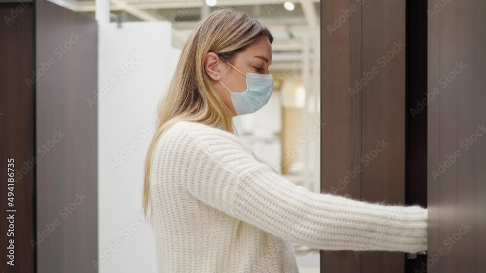 a woman in a protective mask chooses a wardrobe in a furniture store, opens the doors, looks inside a woman in a protective mask chooses a wardrobe in a furniture store, opens the doors, looks inside