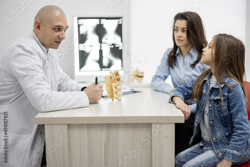 Pediatric orthopedist talking with a little girl and her mom during medical appointment at the office. Concept of pediatrics and examination musculoskeletal child's system
