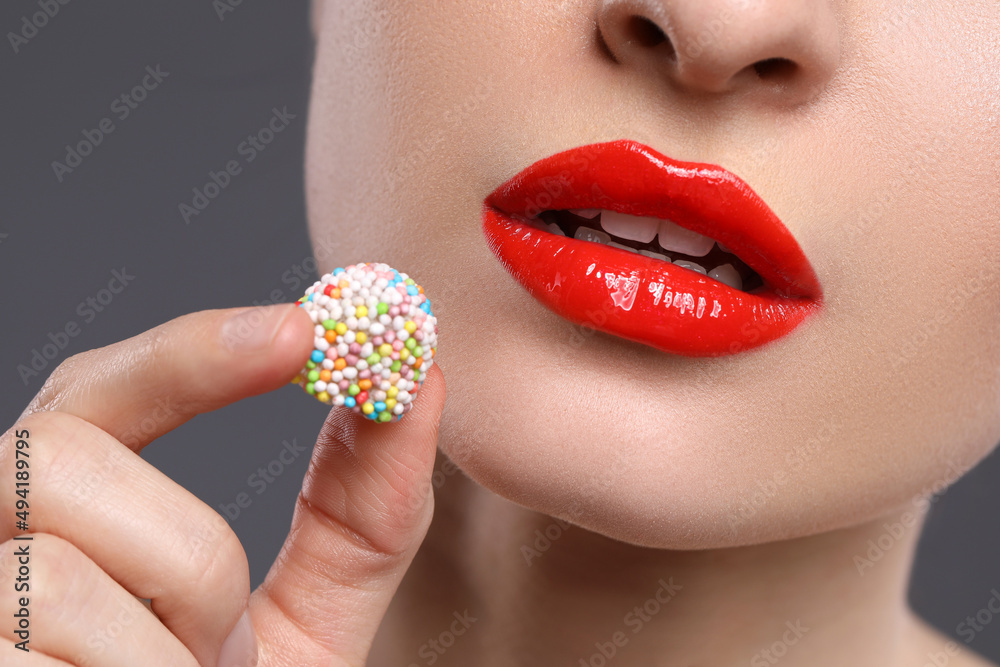 Young woman with beautiful red lips makeup eating candy on grey background, closeup Young woman with beautiful red lips makeup eating candy on grey background, closeup
