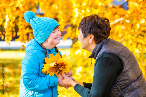 A girl with her mother outdoors in an autumn park collecting a bouquet of fallen leaves