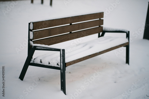 A bench covered with snow. City park empty bench during winter. Concept of empty urban territory covered with snow.