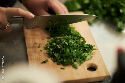 the cook cuts parsley and dill on a wooden board. cooking in a restaurant, chef's hand cutting greens on a wooden board, vegan salad with parsley, vegetable food concept photo