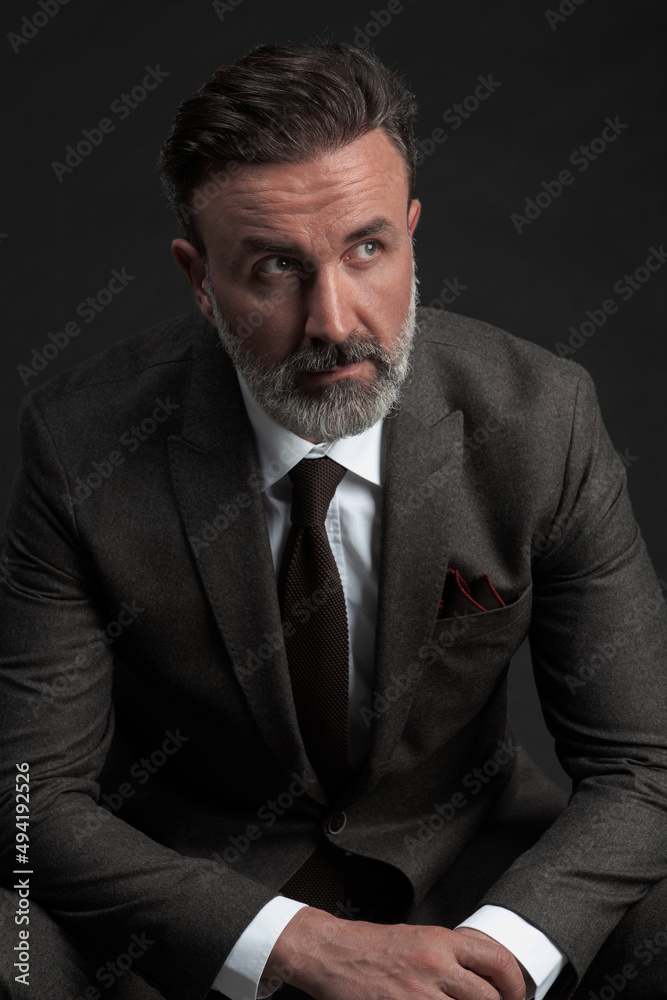 Portrait of a stylish elegant senior businessman with a beard and casual business clothes in photo studio isolated on dark background gesturing with hands Portrait of a stylish elegant senior businessman with a beard and casual business clothes in photo studio isolated on dark background gesturing with hands