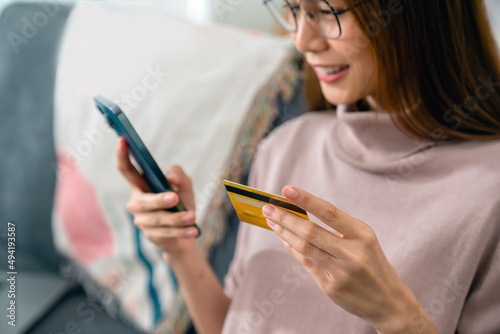 Happy young Asian woman holding credit card and using smartphone for shopping online with payment on internet banking.