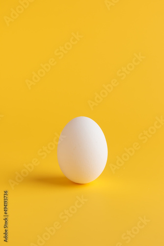 White fresh egg on solid yellow background with shadow, vertical with empty space, Easter holiday symbol, healthy eating concept