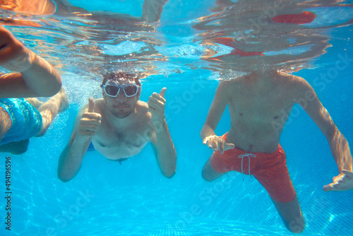 Father With Sons Underwater In Swimming Pool Giving Thumbs Up Gesture