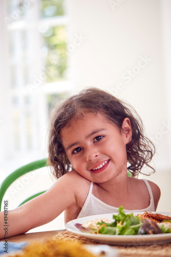 Portrait Of Girl Sitting Around Table At Home With Family Eating Meal Together