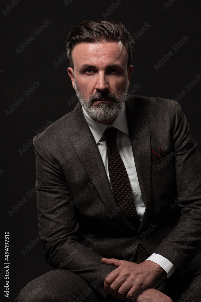 Portrait of a stylish elegant senior businessman with a beard and casual business clothes in photo studio isolated on dark background gesturing with hands Portrait of a stylish elegant senior businessman with a beard and casual business clothes in photo studio isolated on dark background gesturing with hands
