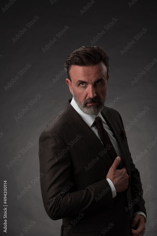 Portrait of a stylish elegant senior businessman with a beard and casual business clothes in photo studio isolated on dark background gesturing with hands Portrait of a stylish elegant senior businessman with a beard and casual business clothes in photo studio isolated on dark background gesturing with hands