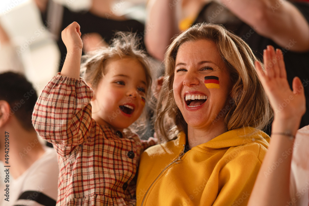 Excited football fans, mother with little daughter, supproting German national team in live soccer match at stadium.