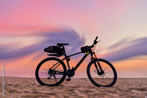 Bicycle on sandy sea coast against backdrop of pink idyllic sunset. Active vacation time © Goffkein