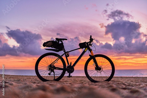 Bicycle on sandy sea coast against backdrop of pink idyllic sunset. Active vacation time