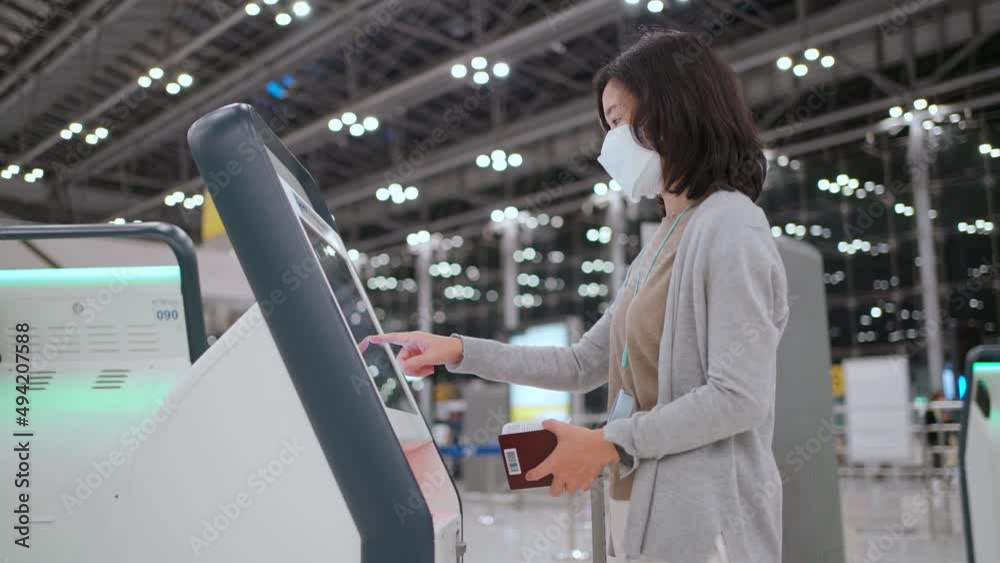 Woman wear mask using self service check-in kiosk at the international airport terminal. Touchscreen and see information on screen. Scan passport to record personal data. New normal travel
