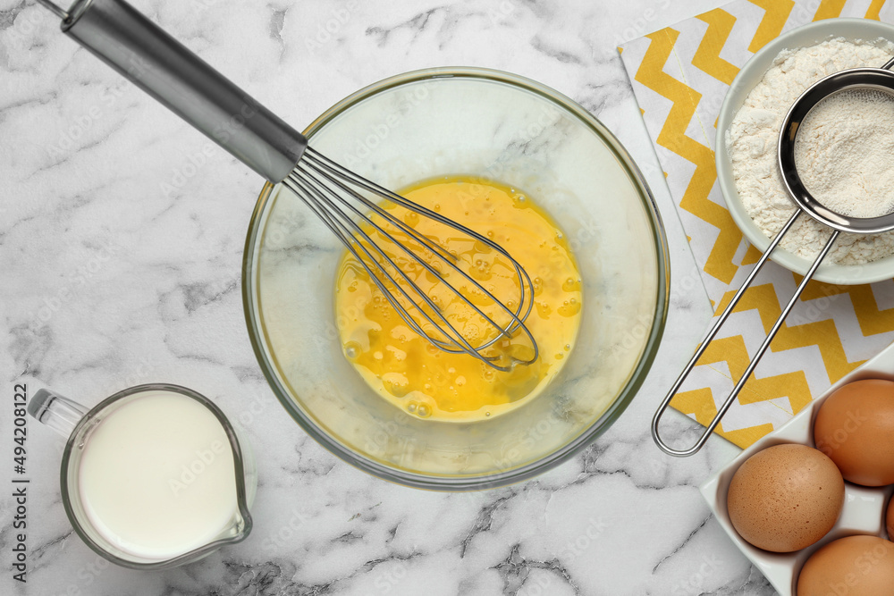 Whisked eggs and other ingredients on white marble table, flat lay Whisked eggs and other ingredients on white marble table, flat lay