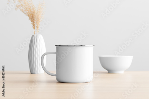 Enamel mug mockup with a dry flower decoration on the wooden table.