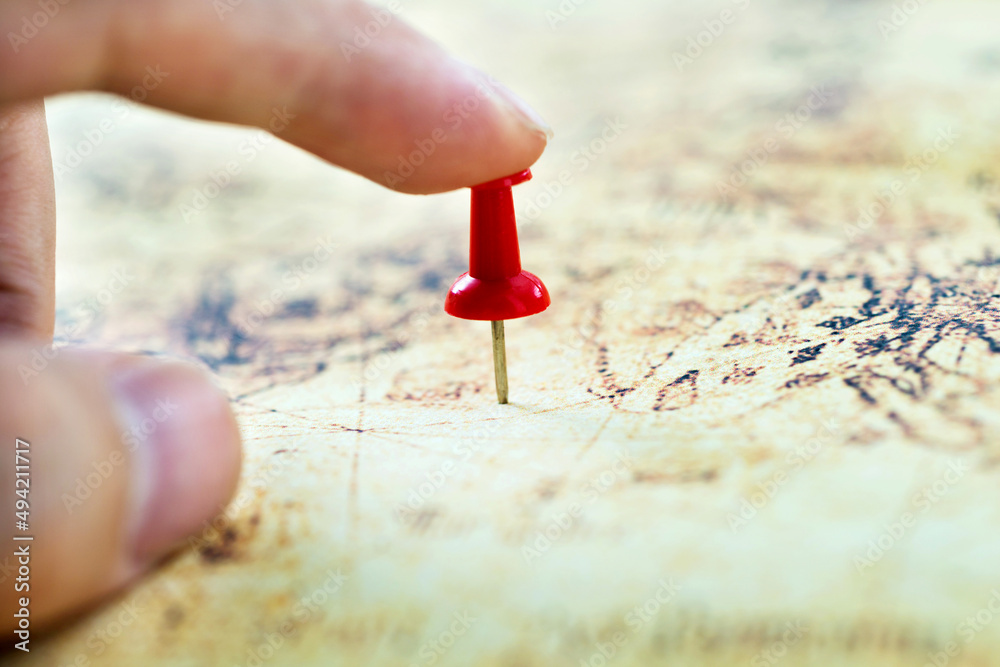 Hand holding red pushpin on map Hand holding red pushpin on map