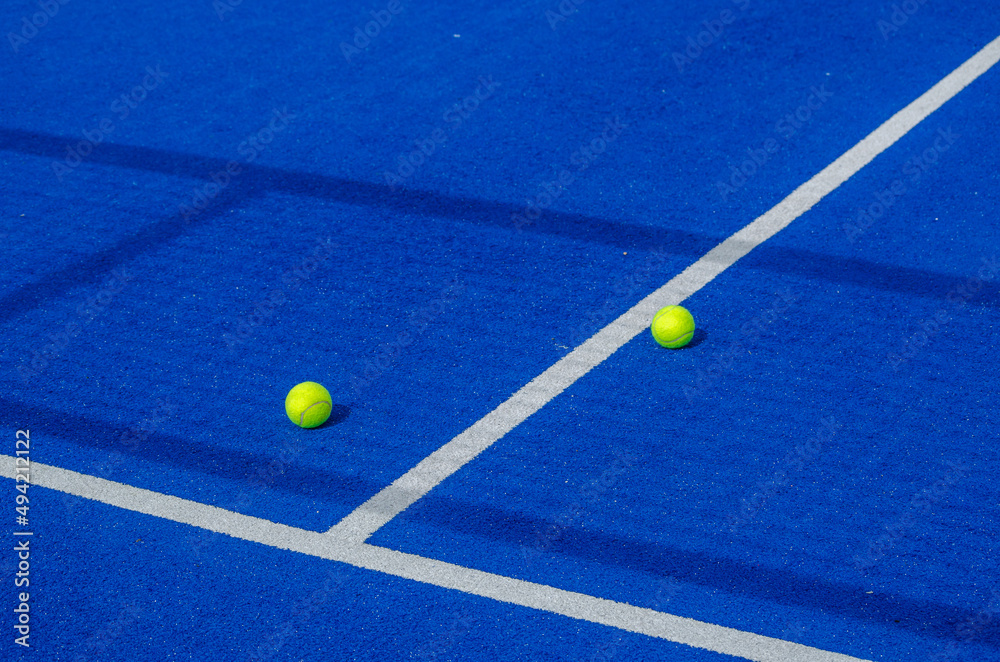 two paddle tennis balls on either side of the center line on a blue paddle tennis court