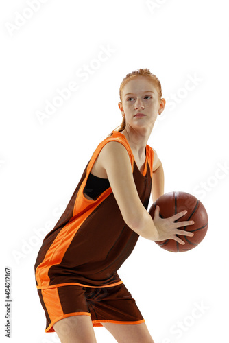 Portrait of young active girl, teenager, basketball player in brown uniform training isolated over white studio background