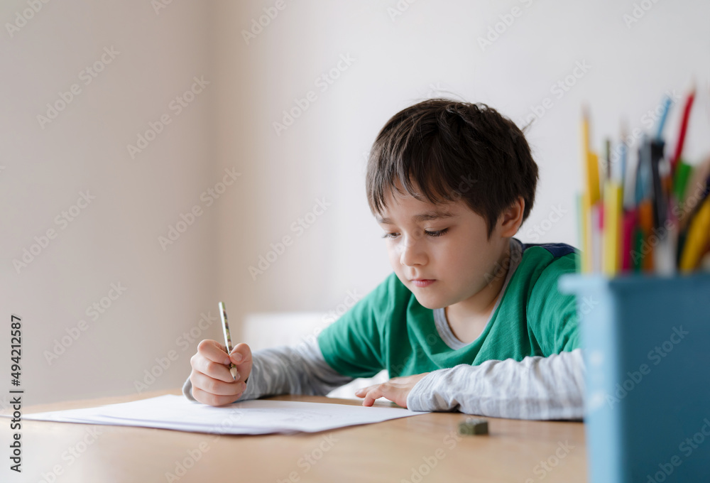 Happy boy using pencil drawing or sketching on paper, Portrait kid siting on table doing homework, Child enjoy art and craft activity at home, Education concept Happy boy using pencil drawing or sketching on paper, Portrait kid siting on table doing homework, Child enjoy art and craft activity at home, Education concept