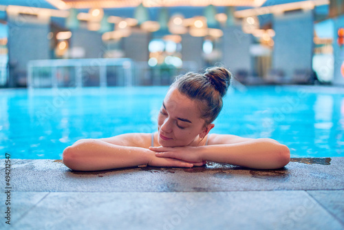 Young serene female dreamer chilling and relaxing alone in swimming pool water in fitness spa center. Mind health and getaway