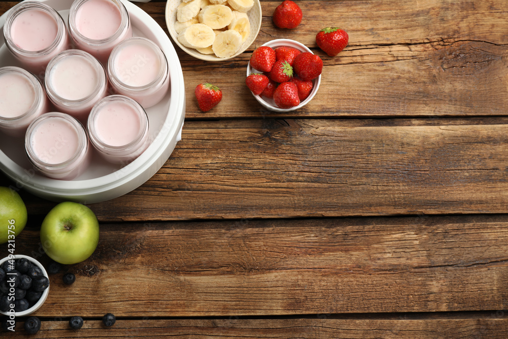 Modern yogurt maker with full jars and different fruits on wooden table, flat lay. Space for text Modern yogurt maker with full jars and different fruits on wooden table, flat lay. Space for text