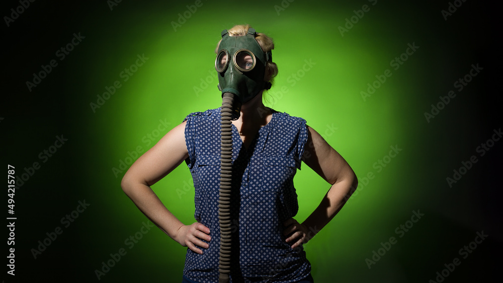 blonde woman in a gas mask put her hands on her hips on a dark dramatic background, hard light