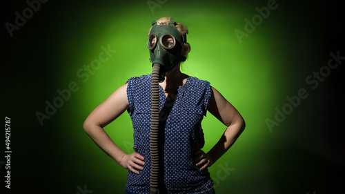 blonde woman in a gas mask put her hands on her hips on a dark dramatic background  hard light