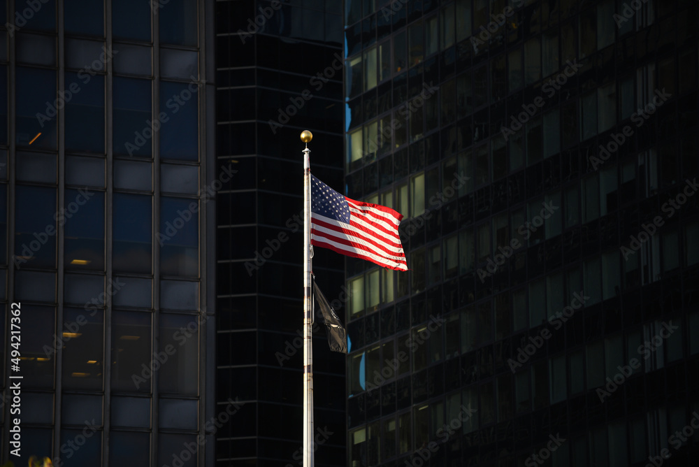 The national flag of the United States of America waving in dramatic sun light between the tall skyscrapers in Manhattan, New York.