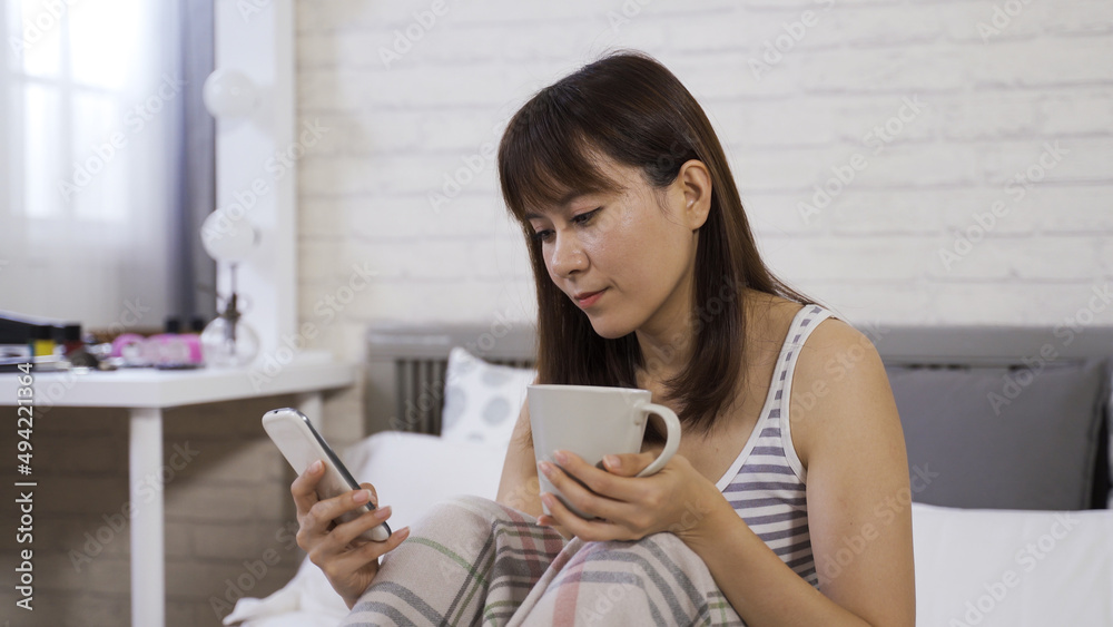 portrait cheerful asian korean woman drinking cup of coffee and using mobile phone while phubbing in leisure at home. portrait cheerful asian korean woman drinking cup of coffee and using mobile phone while phubbing in leisure at home.