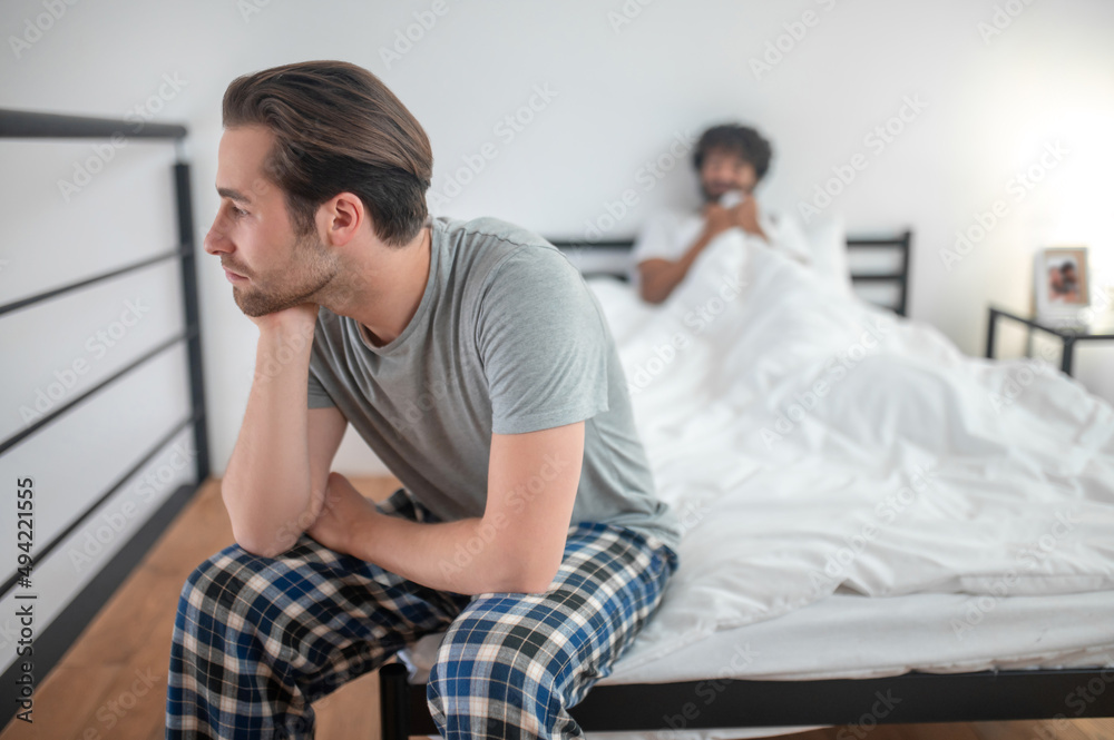 Obraz premium Low-spirited guy seated in the bedroom away from his partner