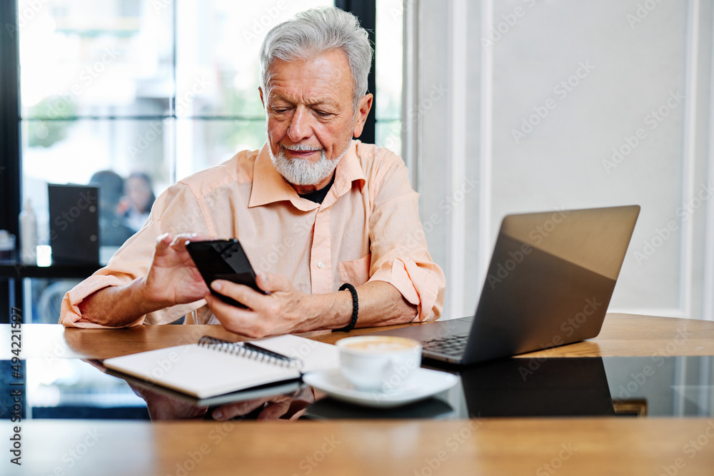 A senior student is sitting in a cafe and using his phone to check up on updates related to school. On the table are a laptop and notebook. A senior student is sitting in a cafe and using his phone to check up on updates related to school. On the table are a laptop and notebook.