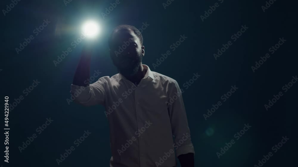 Young person sitting in the dark and using flashlight to search around, looking for evidence. Male detective taking risk and holding lantern to investigate and examine creepy sound.