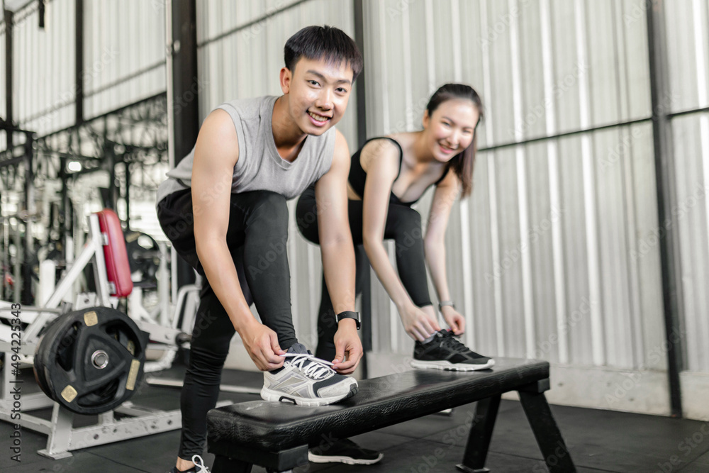 exercise concept The man and woman in the sport club resting one of their feet on the black bench and trying to tie up their shoelace