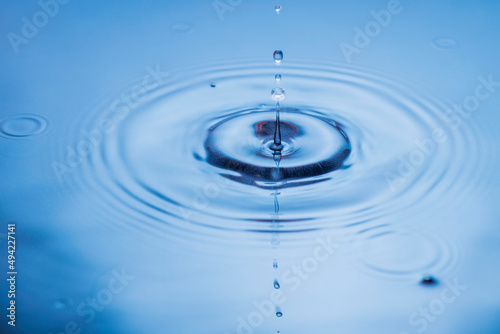 Close up view of falling drops on blue water surface isolated on background.