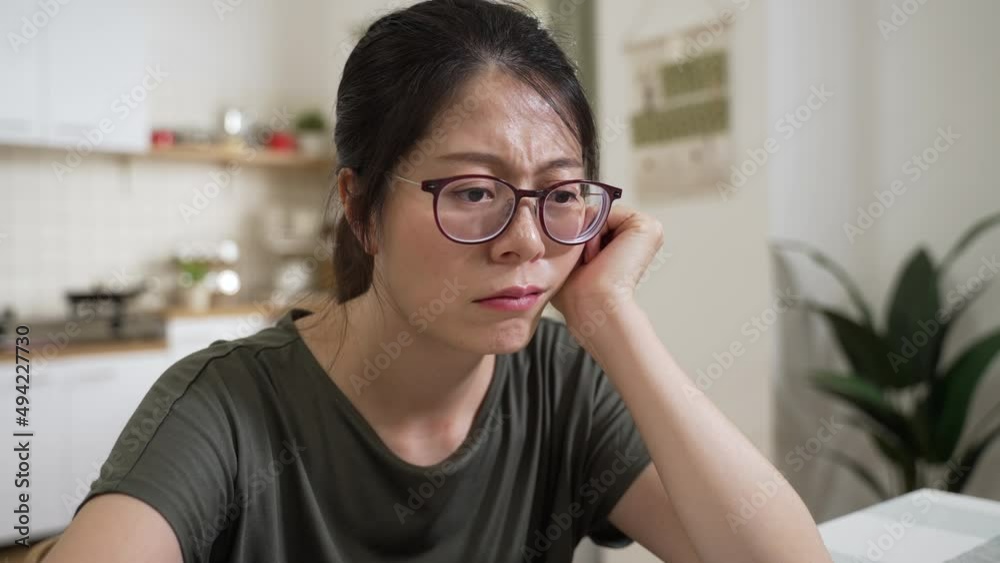 closeup shot of a depressed asian woman propping face and looking at empty space while worrying about unpaid household bill at home. closeup shot of a depressed asian woman propping face and looking at empty space while worrying about unpaid household bill at home.