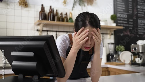 closeup stressed Chinese coffee shop owner is bending over the counter and propping face worrying about business after checking order on the cashier machine.