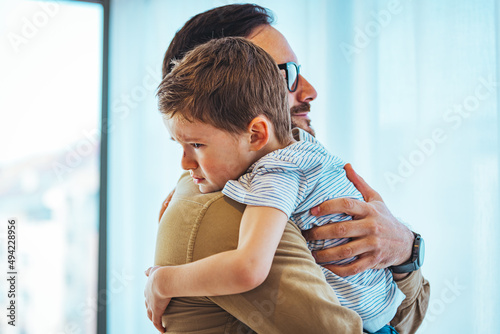 Portrait of a crying child on hands a father. Little boy crying on father's shoulder. Father and Son Together. Close up of small boy crying in his father's hug at home. photo