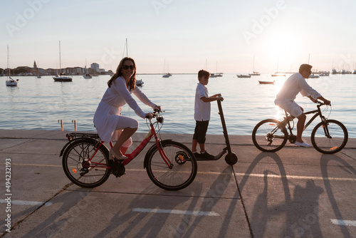 Happy family enjoying a beautiful morning by the sea together, parents riding a bike and their son riding an electric scooter. Selective focus 