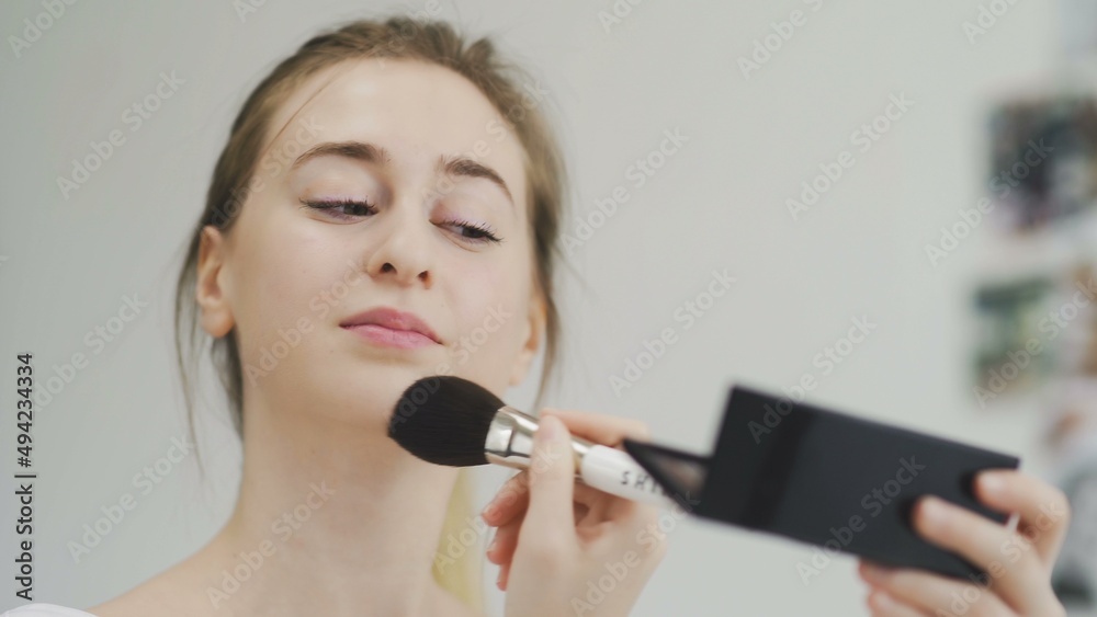 A young woman does her makeup while looking in a small mirror