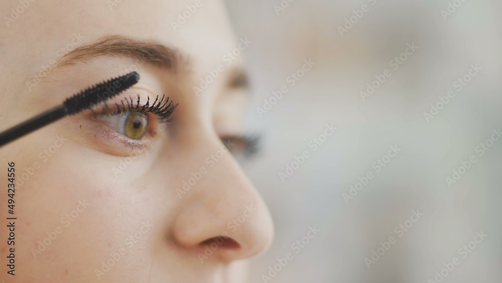 Fototapeta premium Make-up on the face. Close-up of a young woman painting her long eyelashes with black mascara.