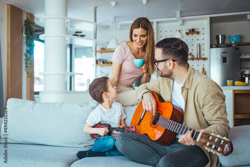Naklejka premium Father teaching his son how to play guitar. Mom watching. Dad playing some music on a guitar to his son. Playing his favorite song. Father Teaching Son Guitar