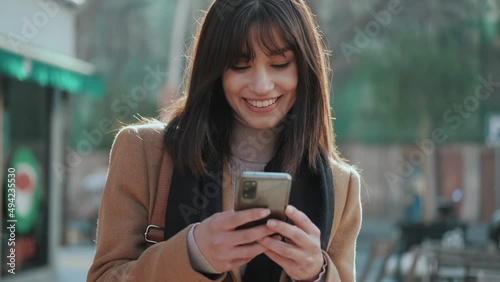 Video of pretty young woman using her mobile phone while drinking cup of coffee walking the streets of the city.