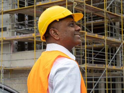 Profile portrait of a smiling Indian civil engineer or factory worker wearing a safety helmet and looking aside