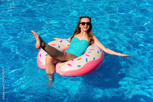 young woman in swimsuit swims on the inflatable water donut in the swimming pool