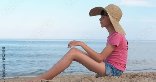 Wallpaper Mural Teen in a hat on the beach. A teen girl sits alone on the beach and watch to the sea water from the beach. Torontodigital.ca