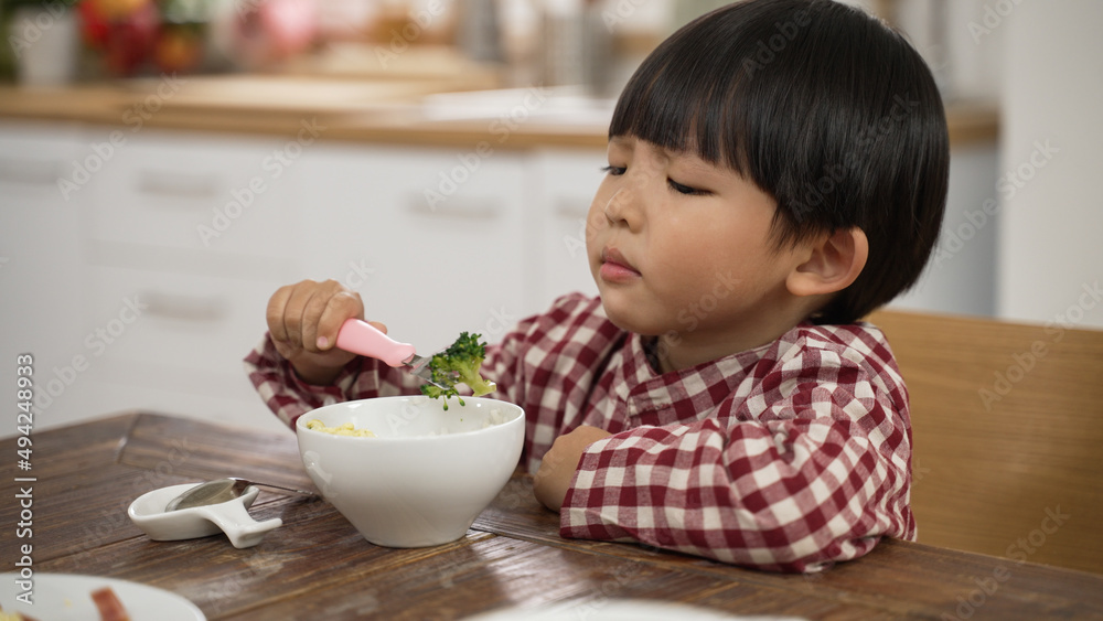 closeup of unhappy Asian little boy making a disgust expression while looking at green vegetable in bowl and shaking head show dislike at dining table closeup of unhappy Asian little boy making a disgust expression while looking at green vegetable in bowl and shaking head show dislike at dining table