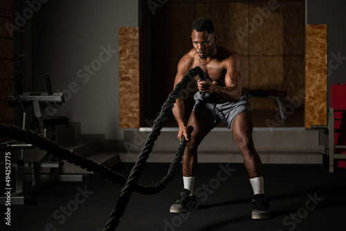 Attractive african american man with naked torso doing endurance exercises with trope. 