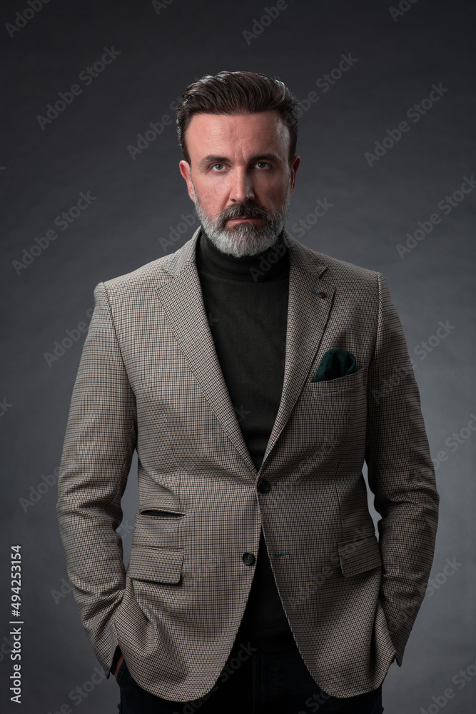 Portrait of a stylish elegant senior businessman with a beard and casual business clothes in photo studio isolated on dark background gesturing with hands